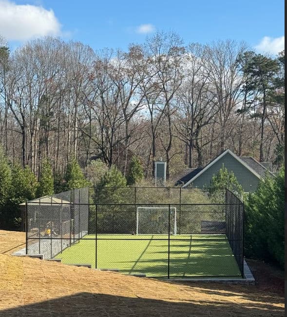 Soccer field with goal, surrounded by trees and a house in the background.