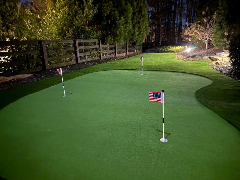 Nighttime view of a backyard putting green with American flag poles.