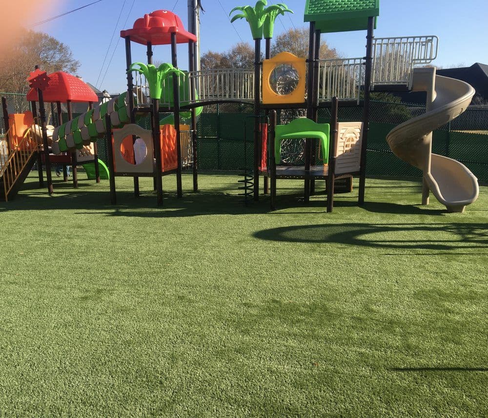 Colorful playground equipment with slides, climbing structures, and soft turf surface.