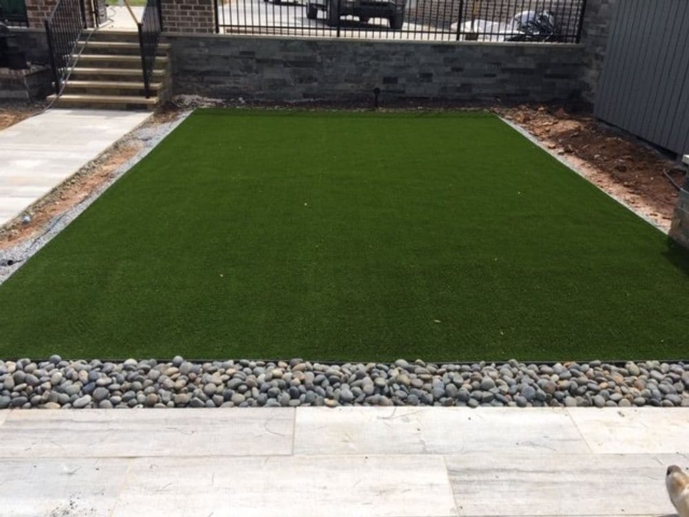 Lush green artificial turf lawn surrounded by decorative stones in a modern backyard setting.