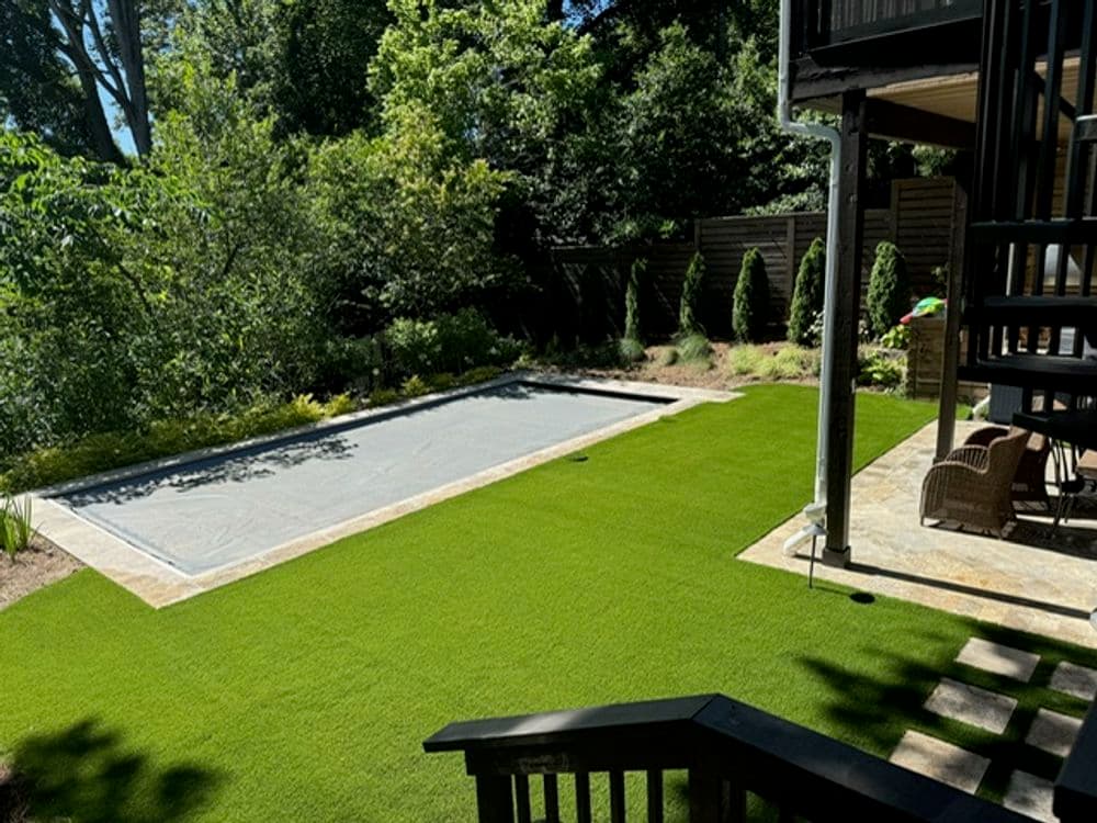 Lush backyard with artificial grass, covered pool, and landscaped greenery.