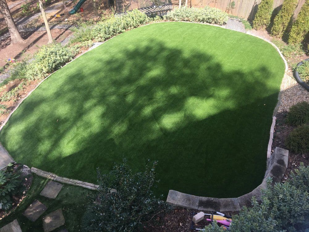 Lush green artificial turf lawn with landscaped edges in a residential backyard.