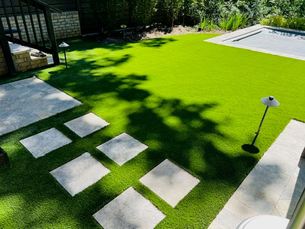 Lush green artificial lawn with stone path and poolside landscaping in a well-maintained garden.