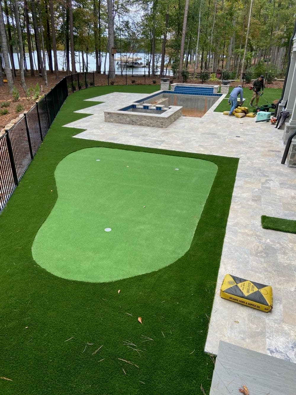 Artificial turf putting green installation beside a pool in a scenic outdoor setting.