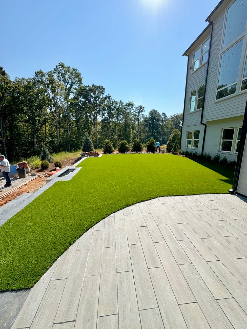 Lush green artificial turf lawn beside modern home with patio and landscaping.