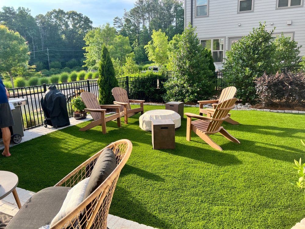 Cozy outdoor patio with Adirondack chairs and artificial grass surrounded by greenery.