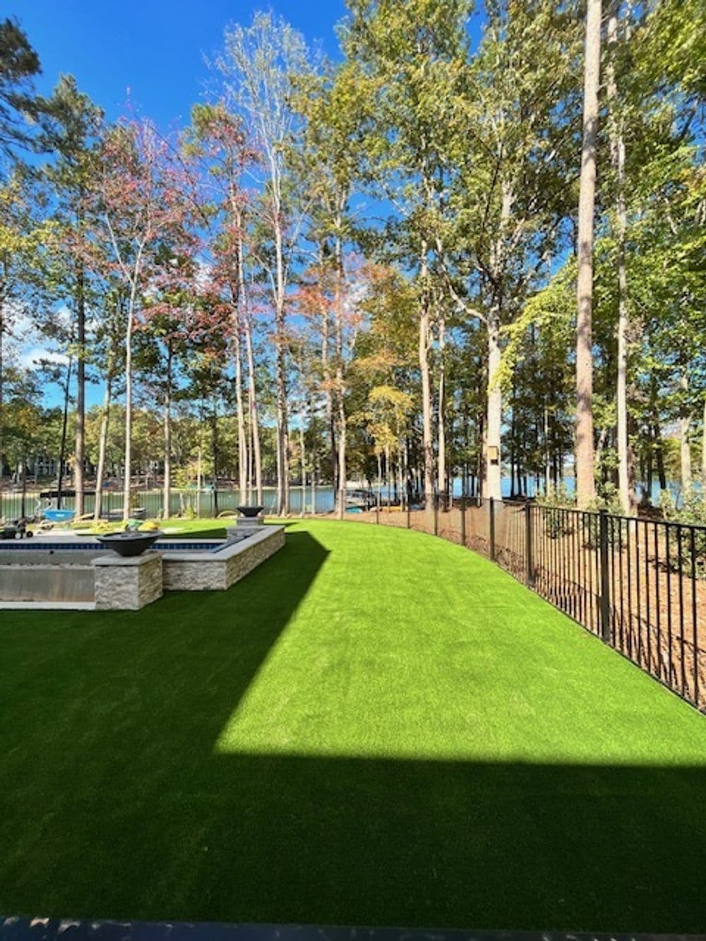 Lush green artificial turf in backyard by lake, surrounded by trees and patio area.