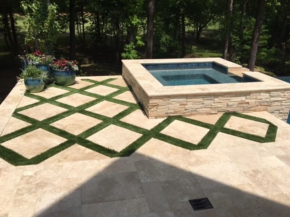 Modern outdoor patio featuring a hot tub surrounded by stone and decorative grass patterns.
