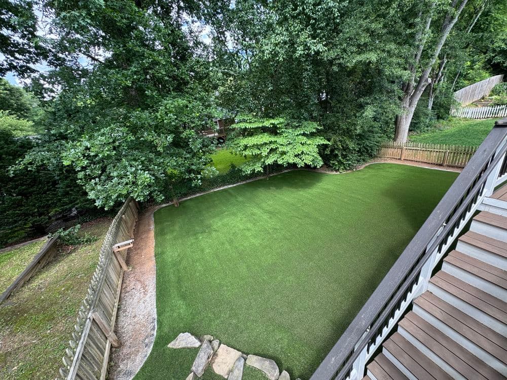 Lush green backyard with artificial turf and trees, viewed from a staircase.