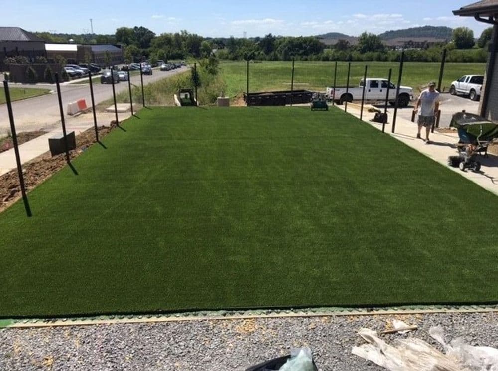 Artificial turf installation on a leveled outdoor area with construction materials nearby.