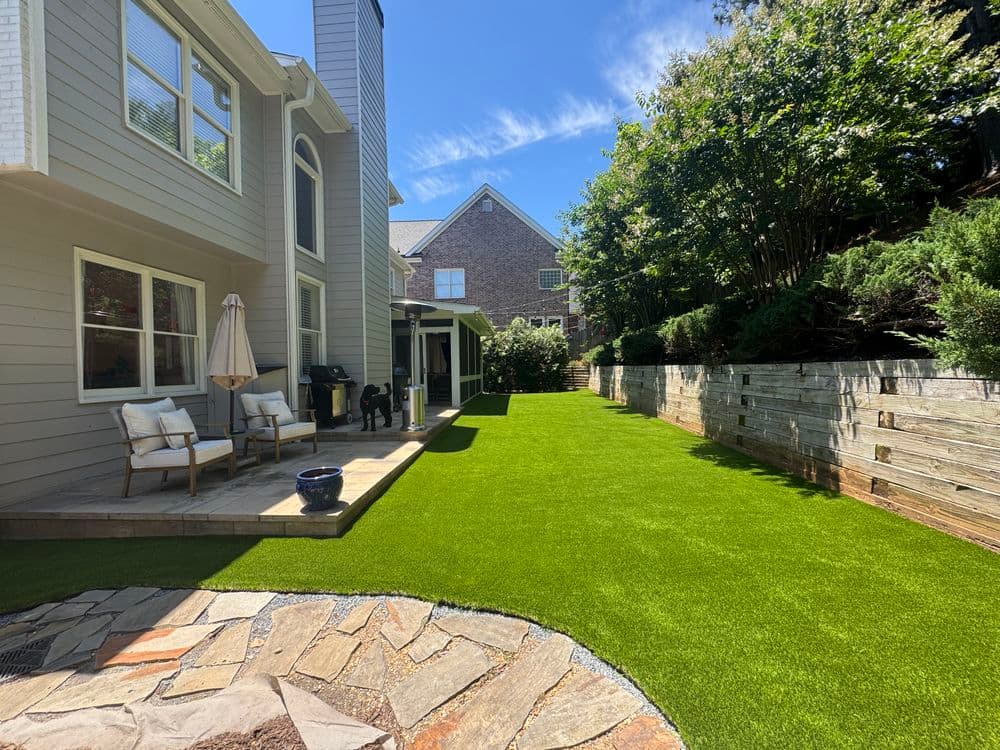 Lush green artificial grass backyard with patio seating and stone pathway in a residential setting.