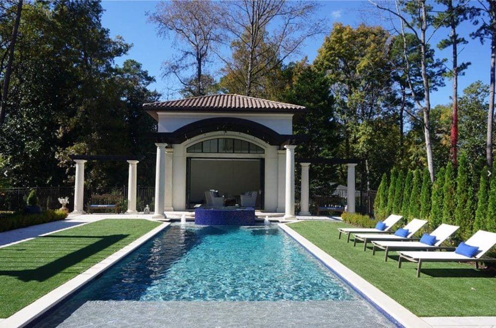 Luxury outdoor pool with modern pavilion and lounge chairs surrounded by lush greenery.