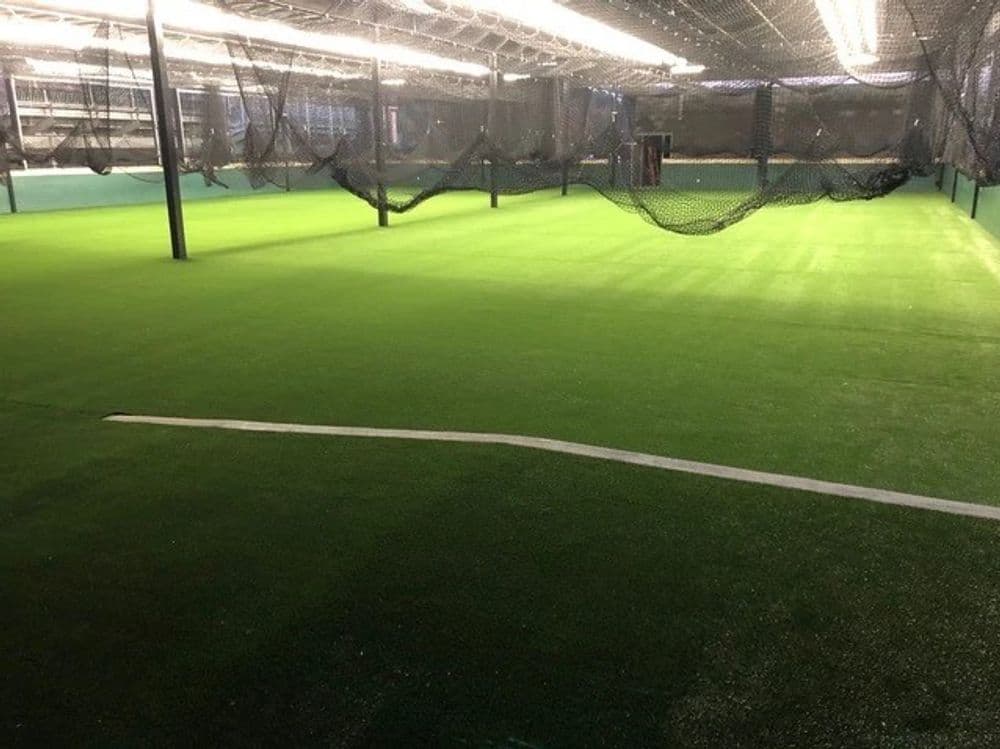 Indoor sports facility with artificial turf and batting cages, well-lit and spacious layout.