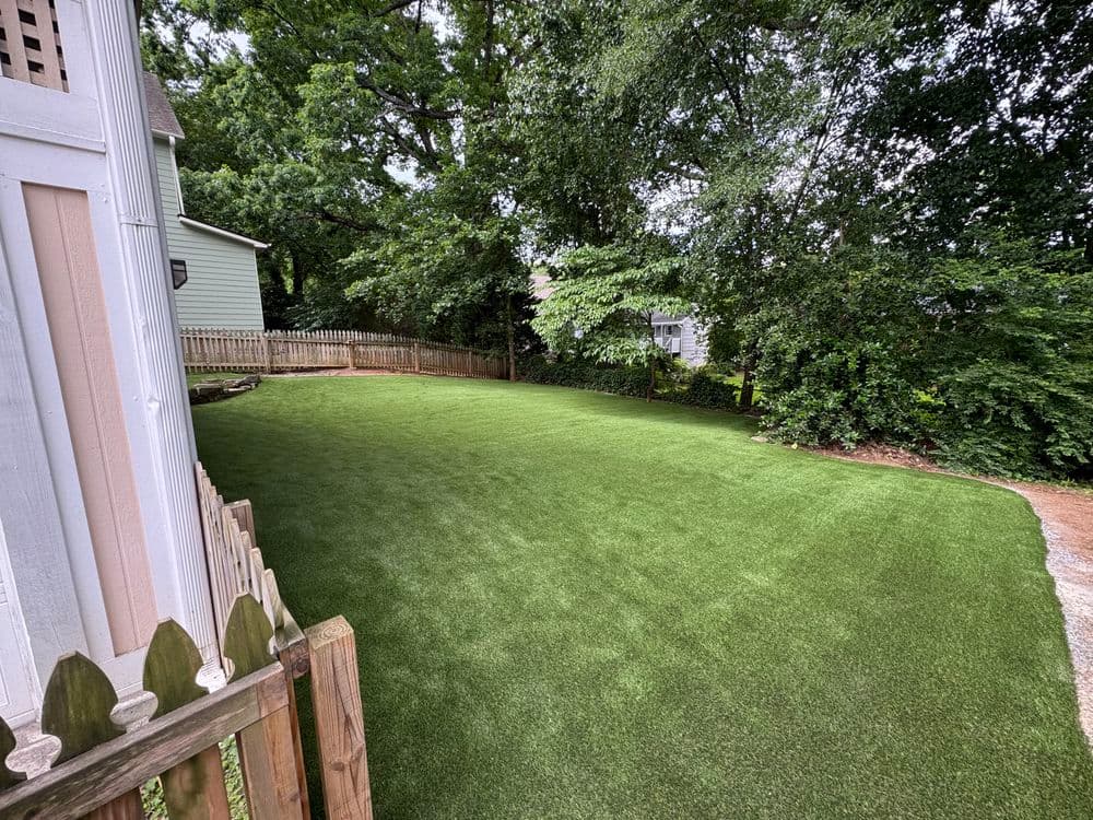 Lush green lawn with trees, fence, and house in a residential backyard setting.