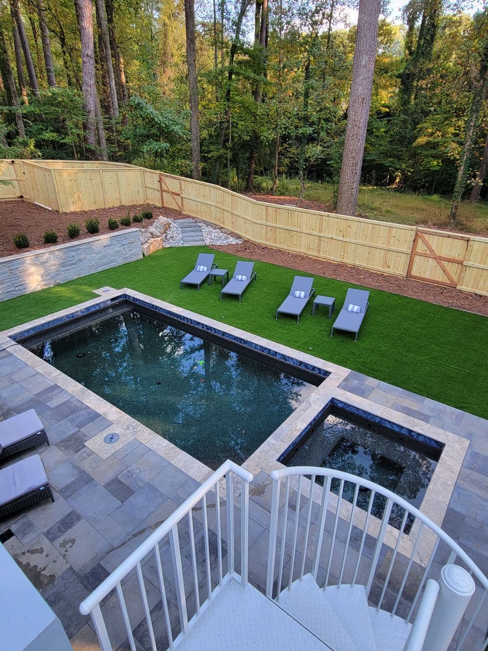 Modern backyard with a swimming pool, lounge chairs, and landscaped greenery in a wooded setting.
