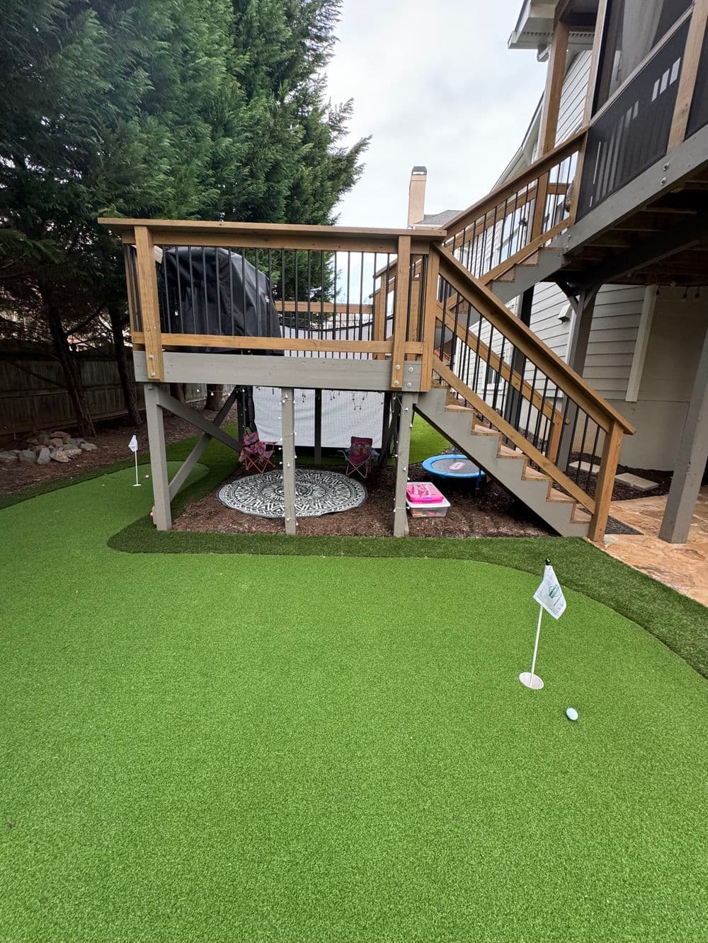 Backyard putting green with stairs, patio, and play area under a deck.