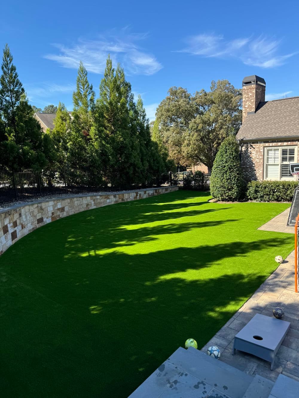 Lush green artificial turf backyard with trees and a stone pathway. Perfect for outdoor activities.
