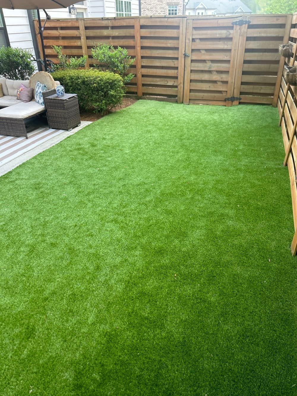 Artificial turf lawn in a landscaped backyard with seating and wooden fence.