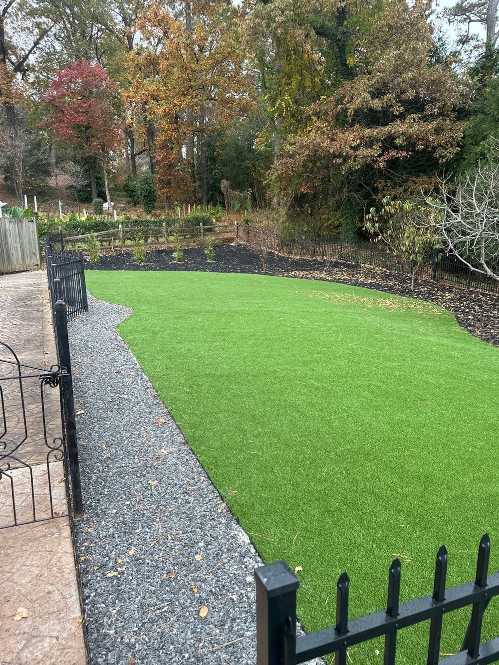 Artificial turf lawn surrounded by decorative gravel and a black fence in a landscaped garden.