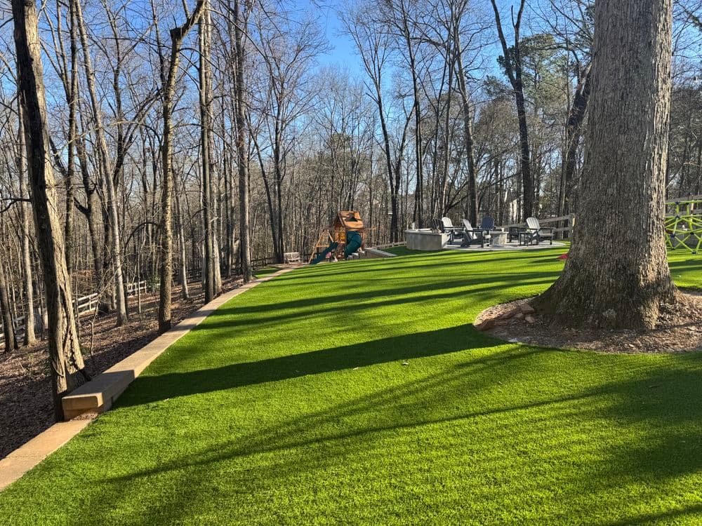 Lush artificial turf landscape with trees, a patio, and play area in a serene outdoor setting.
