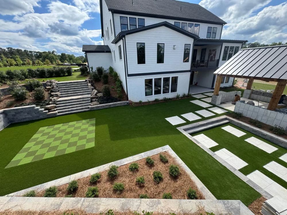 Modern backyard landscape featuring a checkered lawn, stone pathways, and a white house.