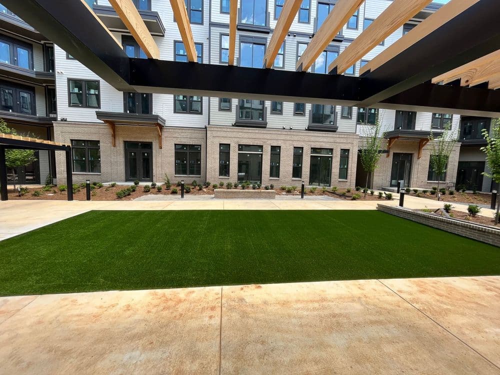 Modern apartment courtyard with artificial grass, landscaping, and shaded seating areas.