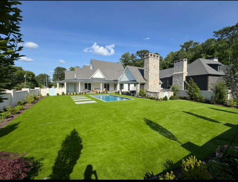 Modern house with pool and manicured lawn, surrounded by lush landscaping and trees.