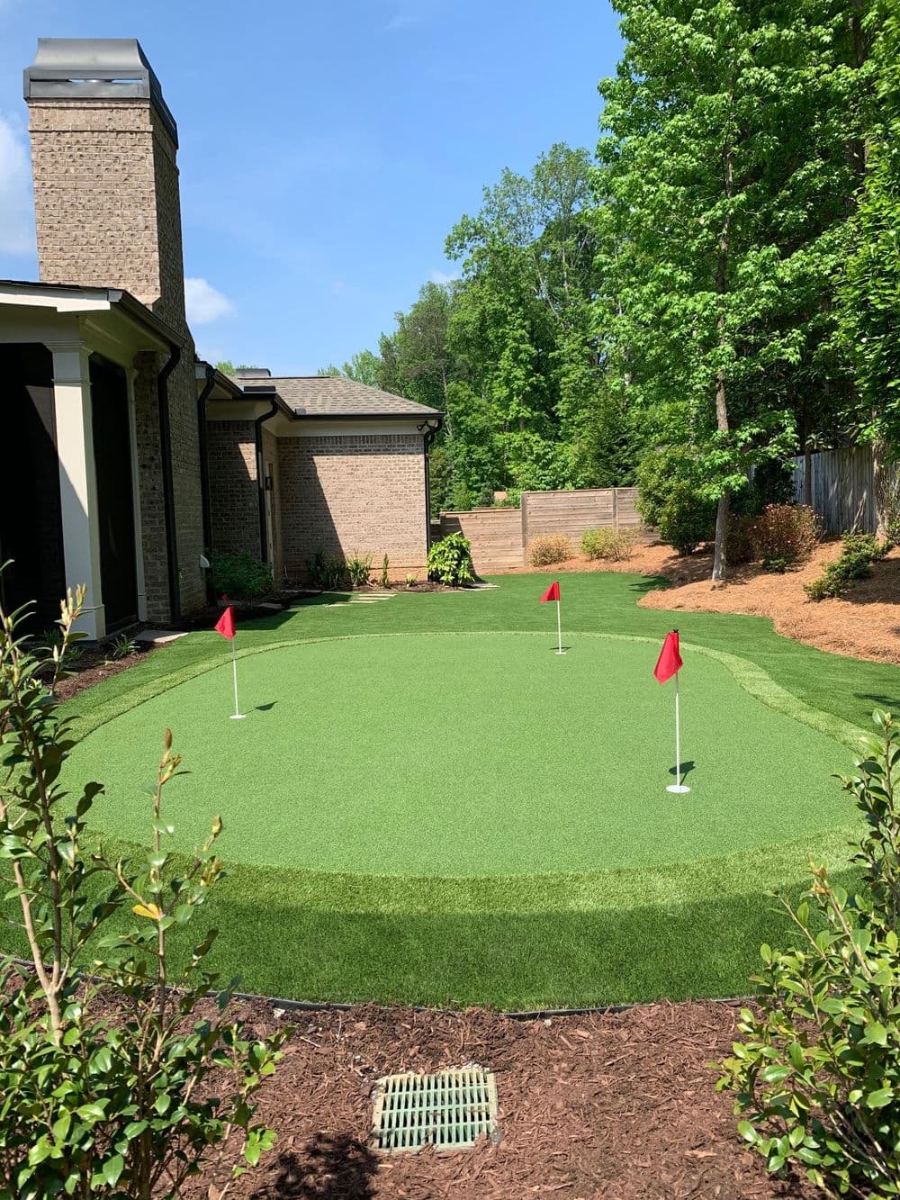 Outdoor artificial putting green with red flags in a landscaped backyard setting.