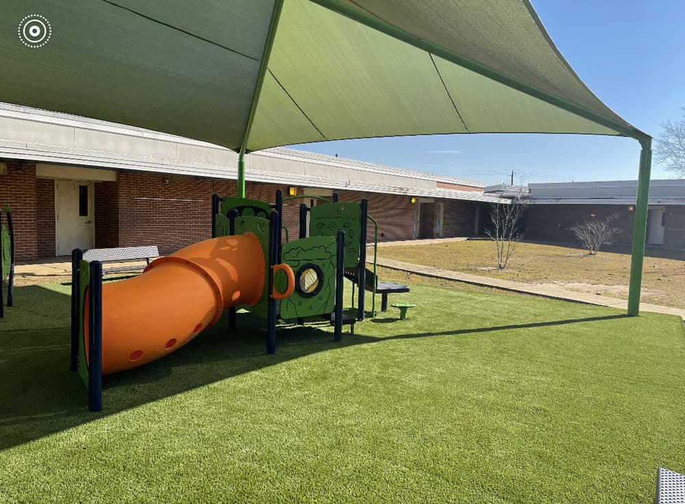 Colorful playground slide under shade in a grassy school courtyard. Safe play area for children.