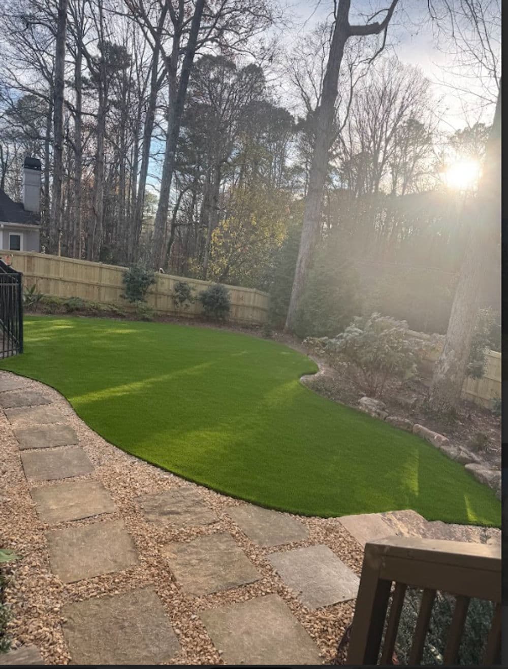 Lush green lawn in a landscaped backyard with trees and sunlight filtering through.