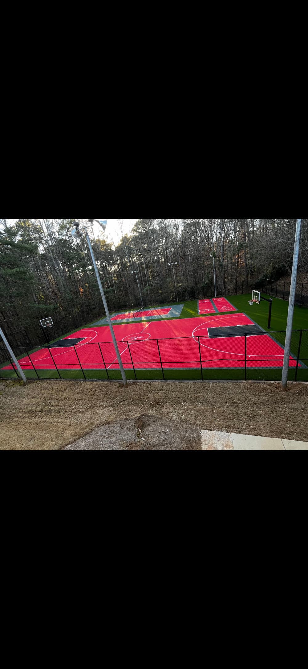 Aerial view of a vibrant red basketball court surrounded by trees and fencing.