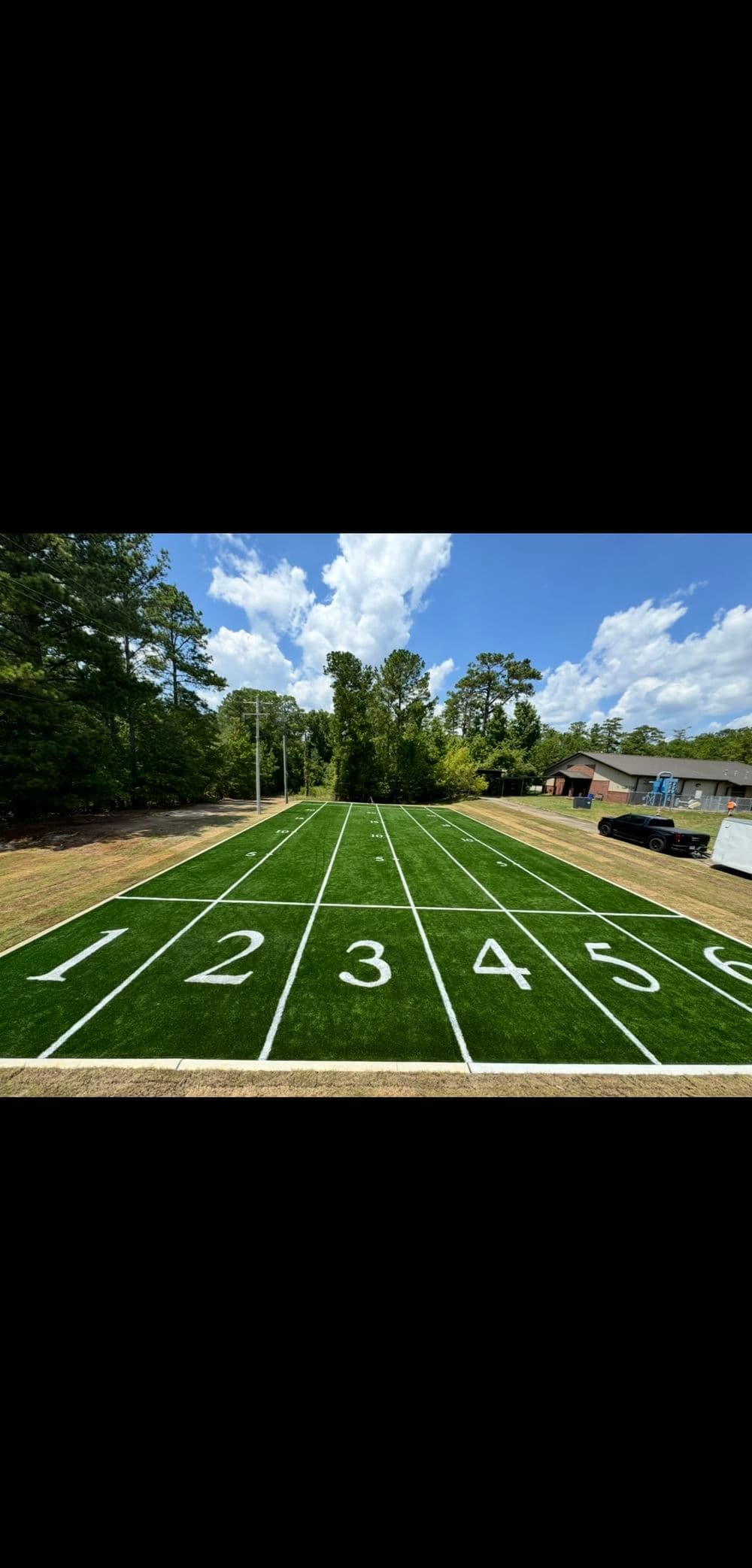 A vibrant football field with yard markers 1 to 6 under a blue sky and green trees.