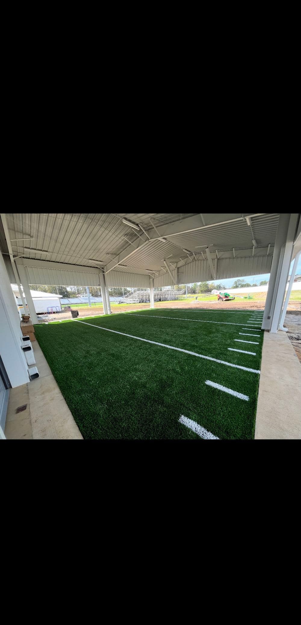 Artificial turf field under a large covered structure, featuring white yard lines.