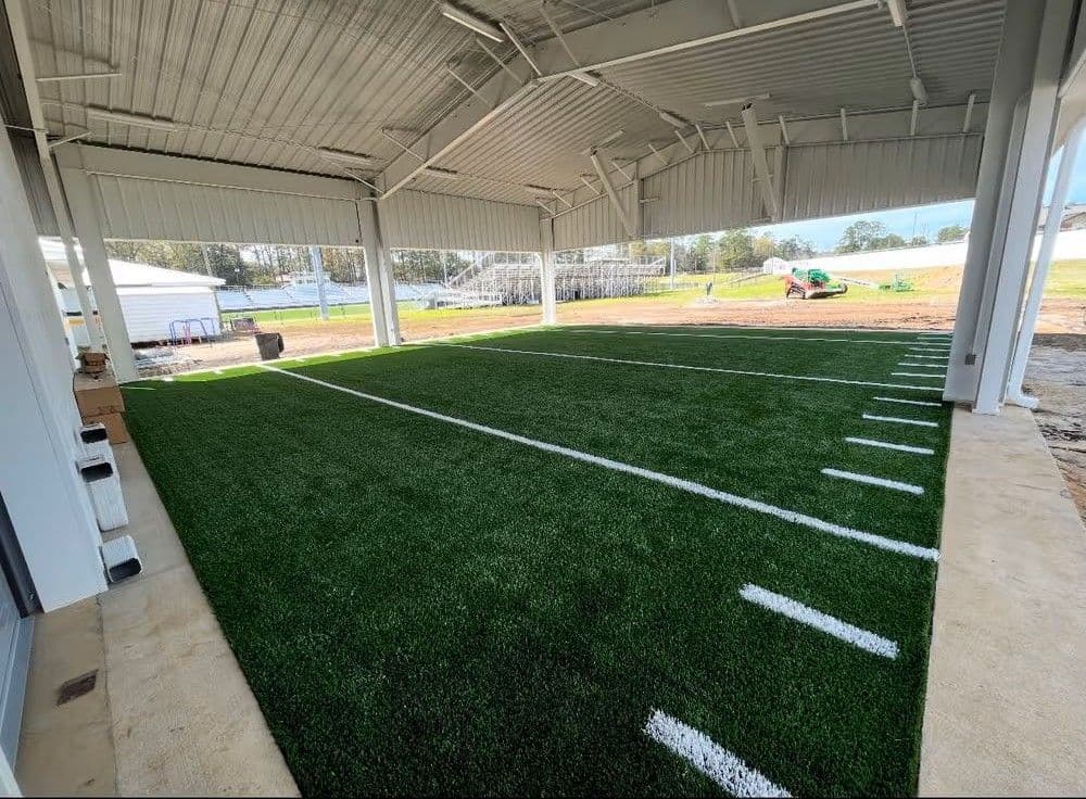 Indoor football training facility with artificial turf and marked yard lines.